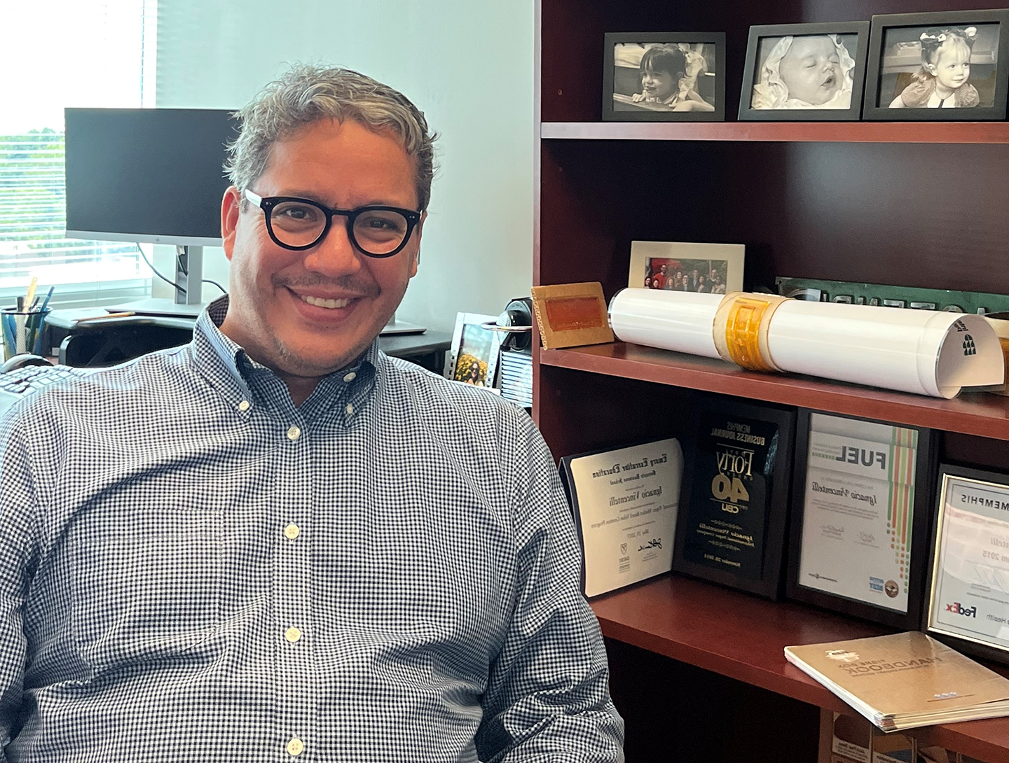 Ignacio smiles at the camera from behind his desk at work with pictures of his kids in the background